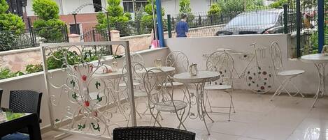 An outdoor seating area with tables and chairs, a decorative fence, and a view of the surrounding buildings.