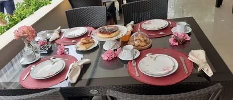 A dining table set with plates, cutlery, and pastries, surrounded by wicker chairs.