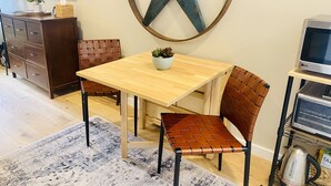Un coin repas avec une table en bois, deux chaises en osier marron, une grande étoile décorative accrochée au mur, une petite plante en pot et un téléviseur posé sur un meuble.