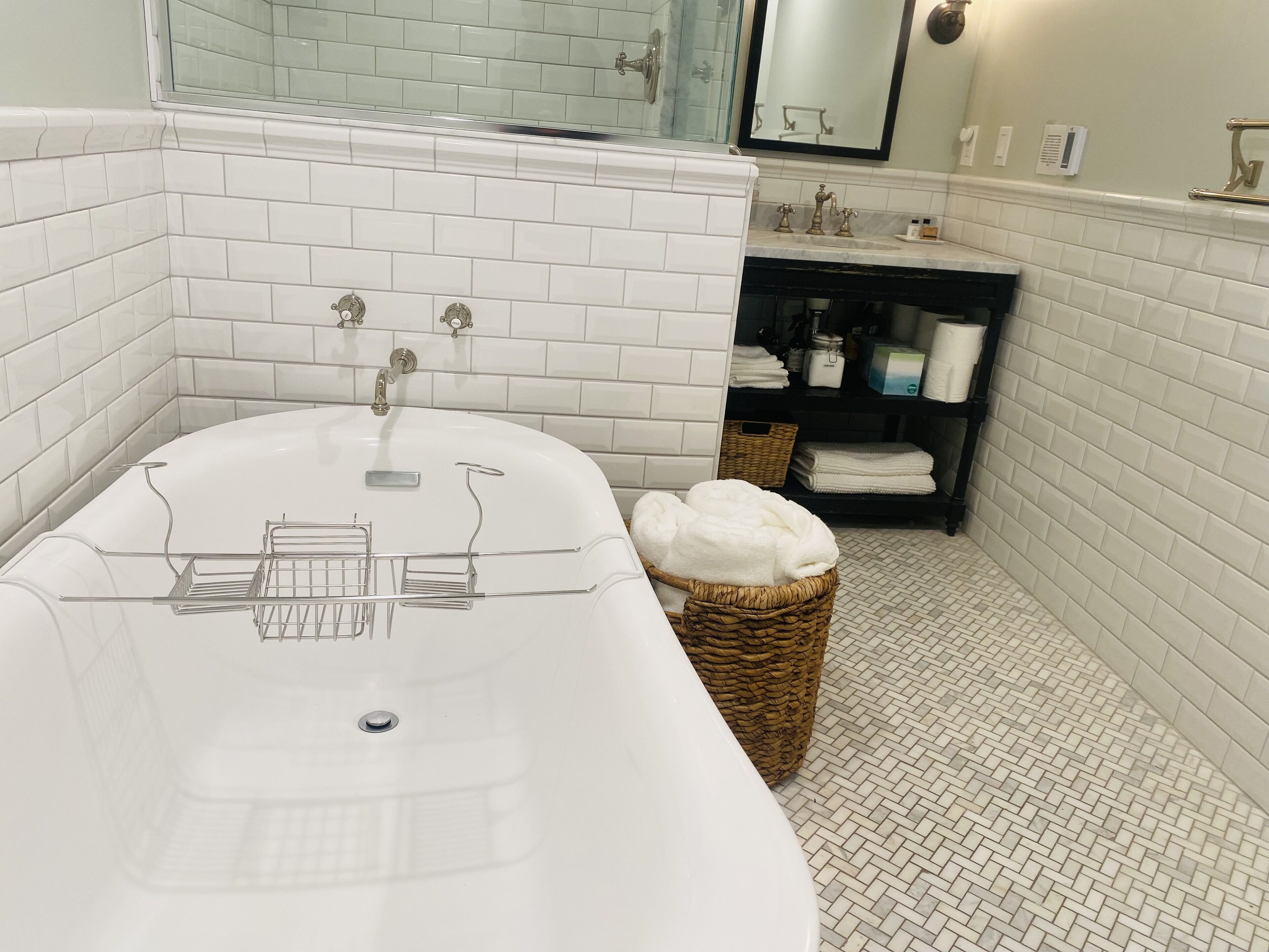 A modern bathroom with a freestanding bathtub, a glass shower enclosure, and a wicker basket filled with towels.