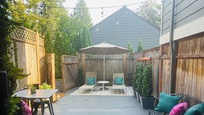 Une terrasse à l’arrière de la maison, avec une table, des chaises et un espace salon abrité.