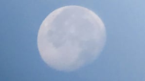 Een volle maan tegen een heldere blauwe lucht.