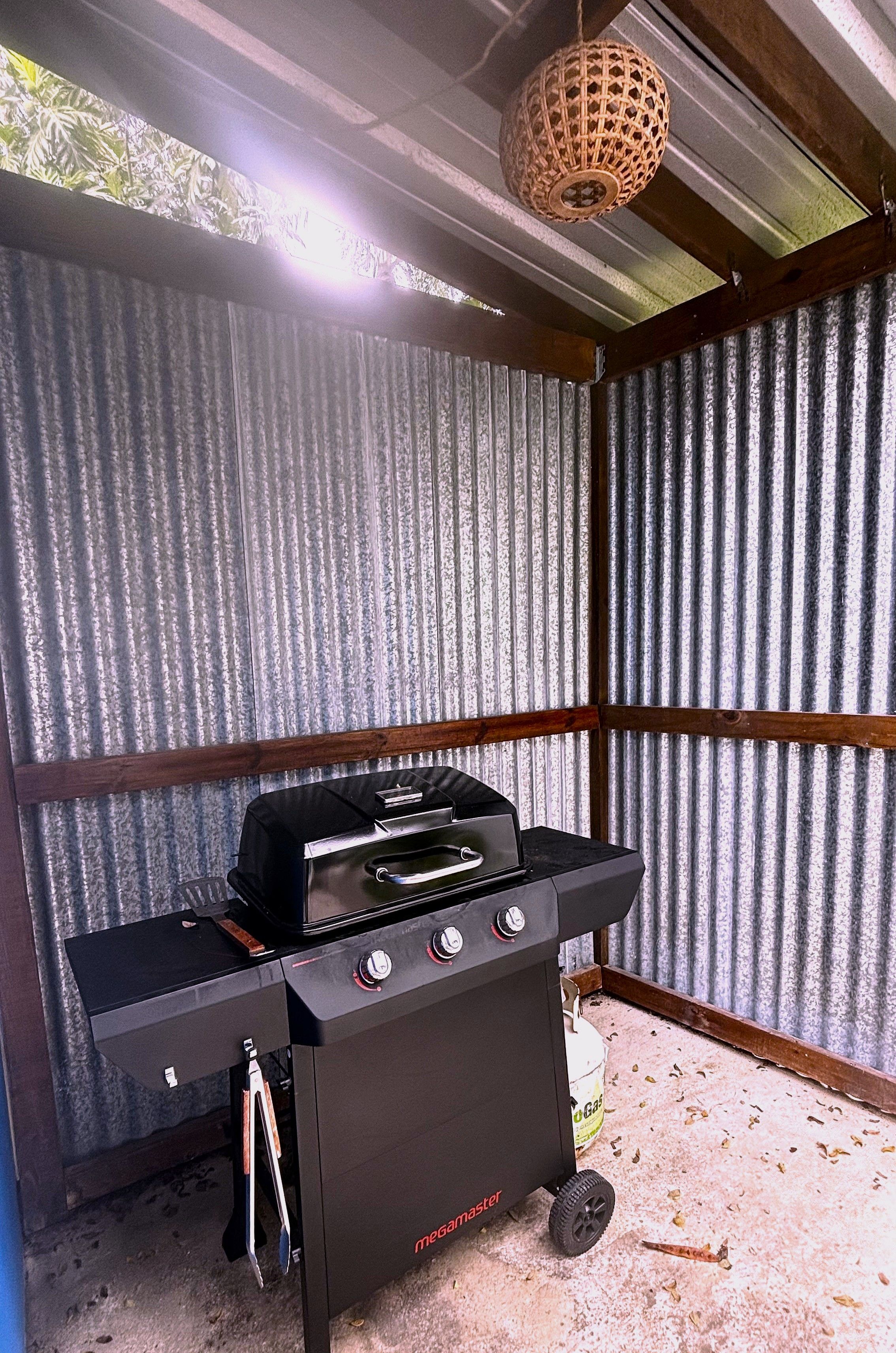 A portable gas grill with wheels, a wooden ceiling, and corrugated metal walls.
