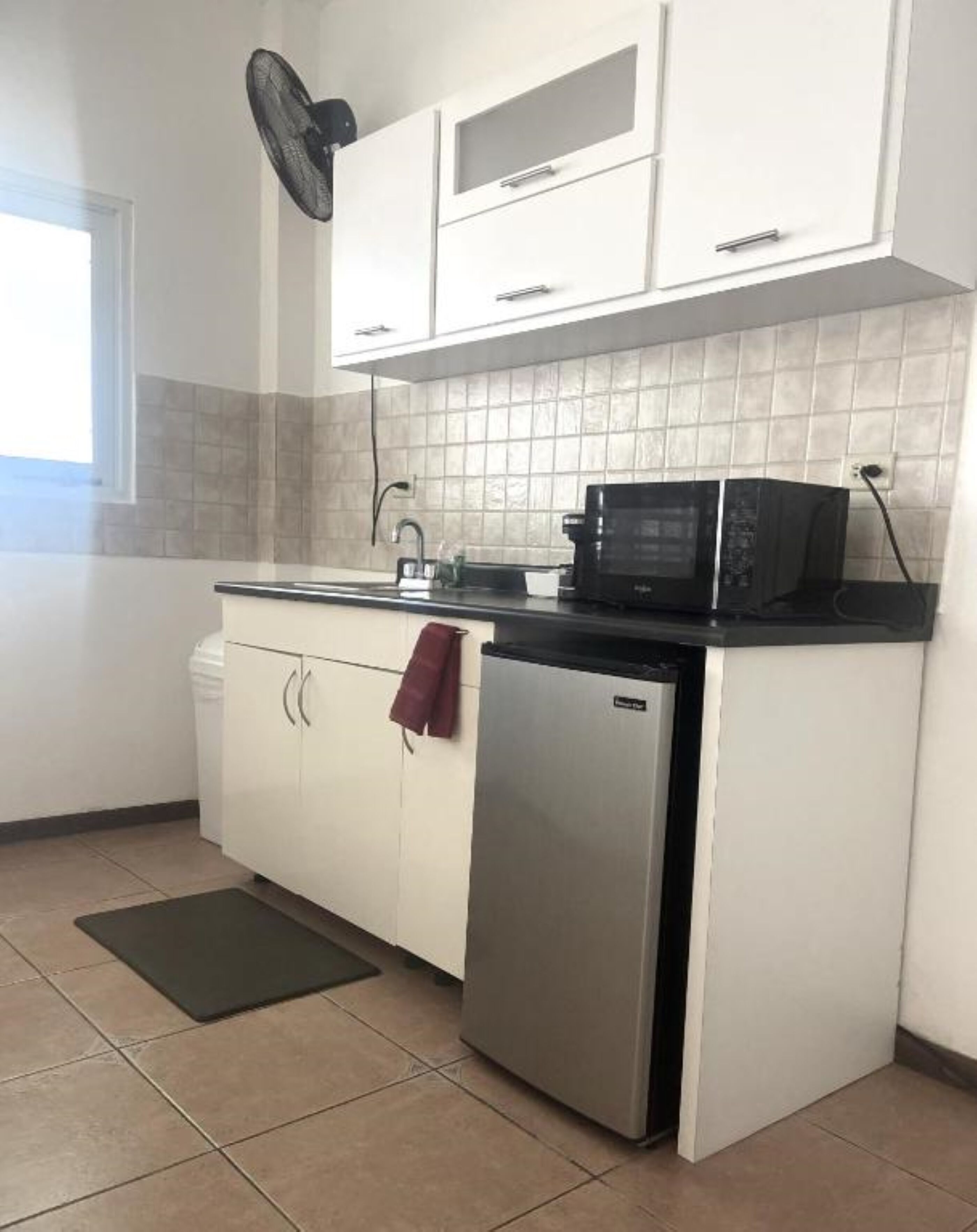 A compact kitchen with white cabinets, a black countertop, a stainless steel refrigerator, and a microwave.
