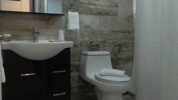 A bathroom with a sink, mirror, toilet, and shower curtain.