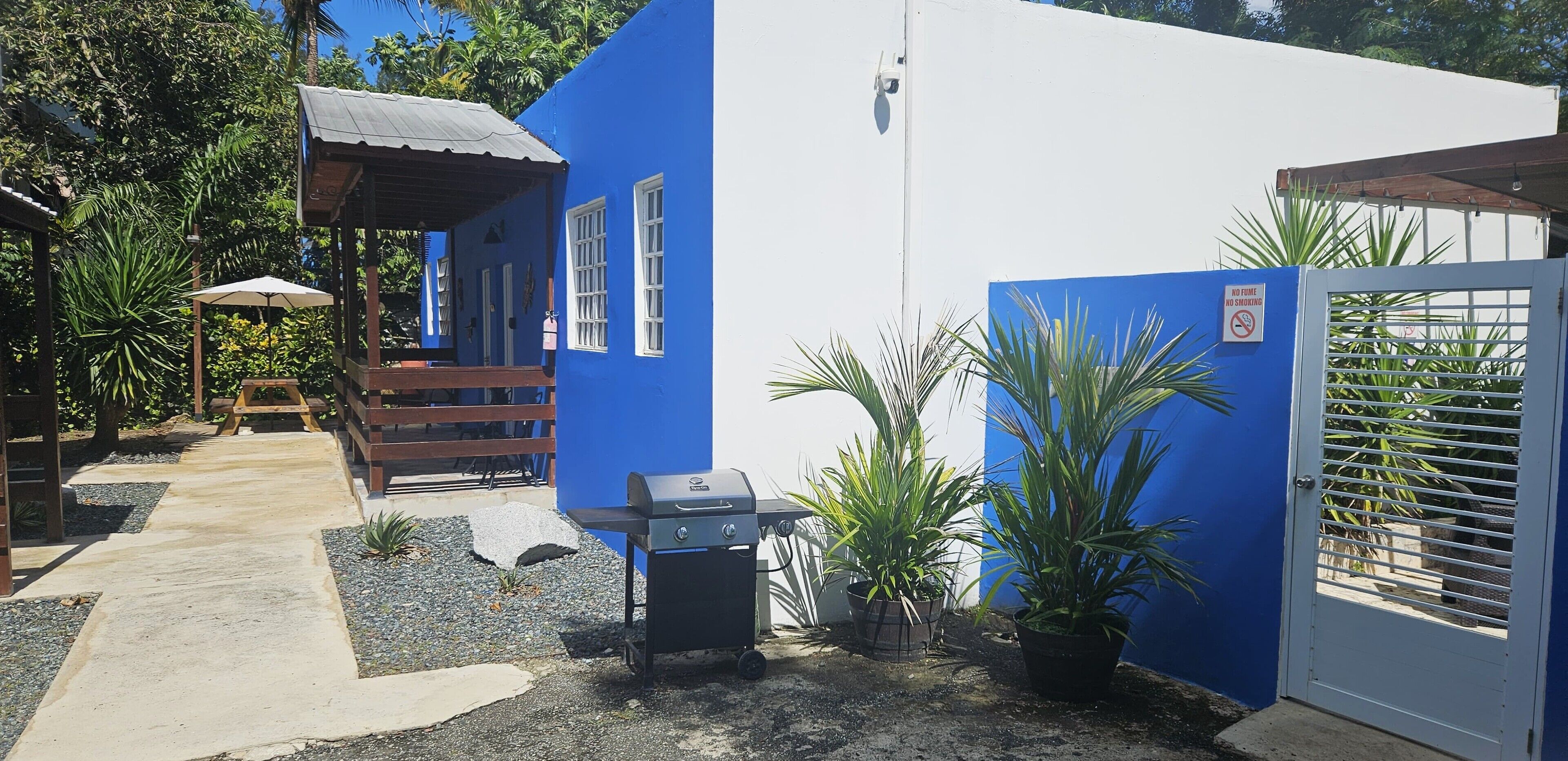A blue building with a barbecue grill, a wooden deck, and a gate with a no smoking sign.