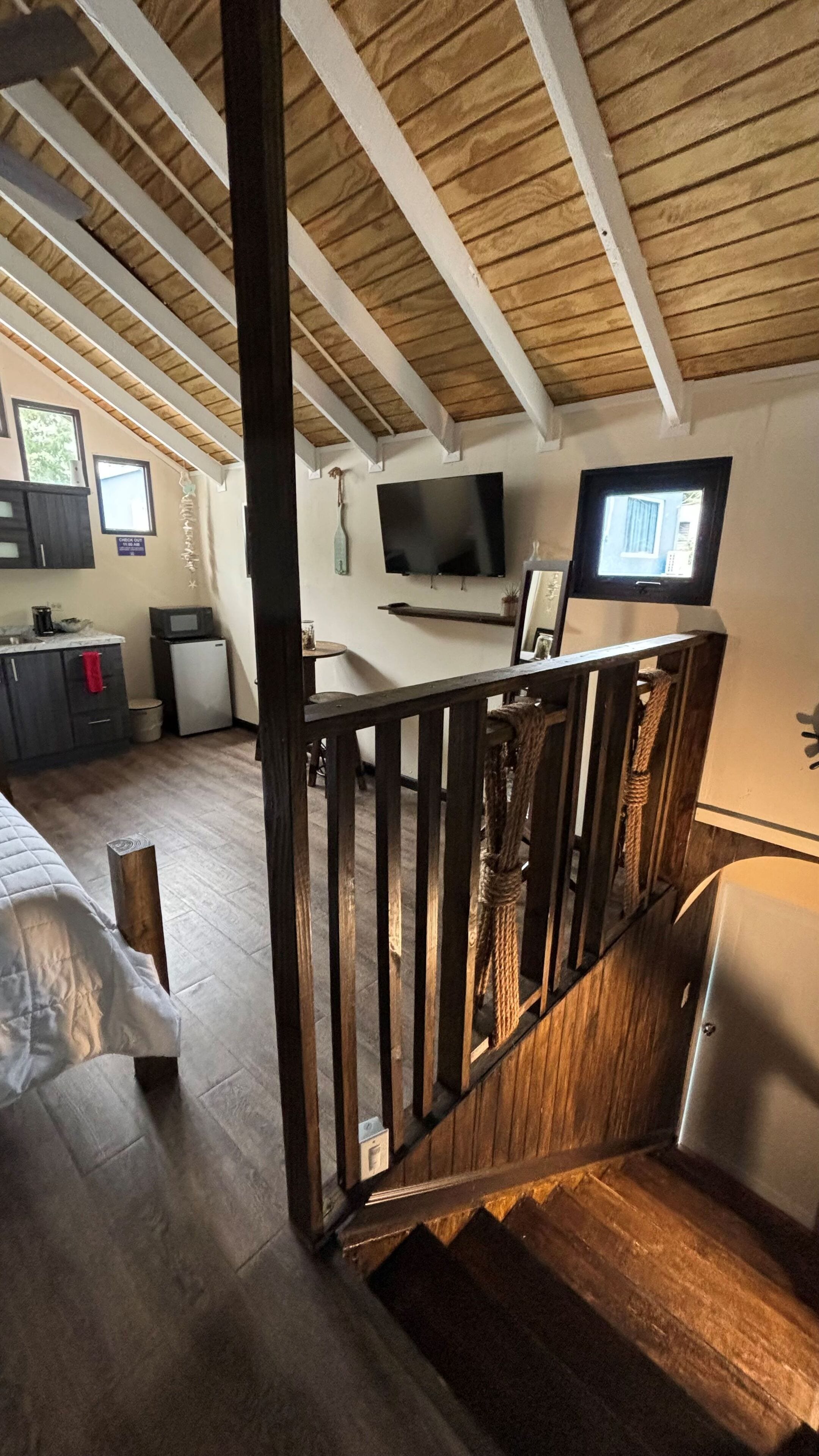 Ein Zimmer mit Holzboden, einem Bett, einem Schreibtisch, einem Fernseher und einer kleinen Küchenzeile.