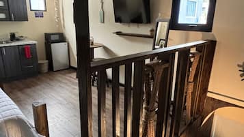 Ein Zimmer mit Holzboden, einem Bett, einem Schreibtisch, einem Fernseher und einer kleinen Küchenzeile.