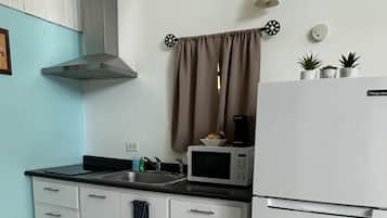 Eine kompakte Küche mit weißen Schränken, einer schwarzen Arbeitsplatte, einer Mikrowelle, einem Spülbecken und einem kleinen Kühlschrank.