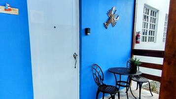 Un mur extérieur bleu avec une porte blanche, une petite table d’extérieur avec deux chaises et un élément décoratif mural.