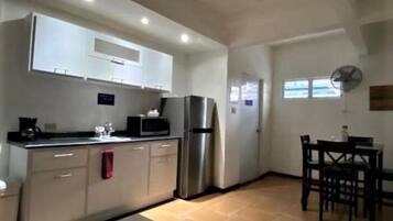 A compact kitchen with white cabinets, a stainless steel refrigerator, a microwave, and a dining area with a table and chairs.