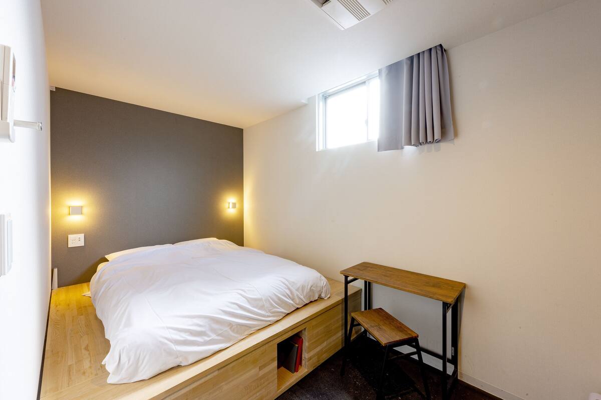 Une chambre à coucher de taille modeste, avec un lit en bois, un petit bureau et une fenêtre avec des rideaux.