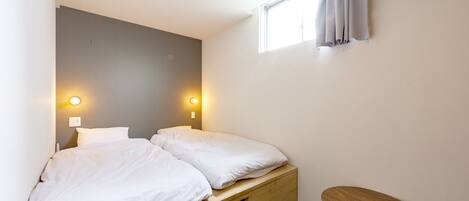 A bedroom with a bed, bedside lamps, a small wooden table, and a window with curtains.
