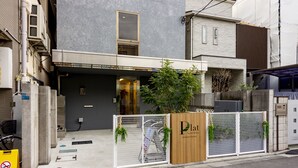 Ein modernes Gebäude mit grauem Fassadenschmuck, einem hölzernen Eingangstor und einem Schild, das es als Hotel kennzeichnet.