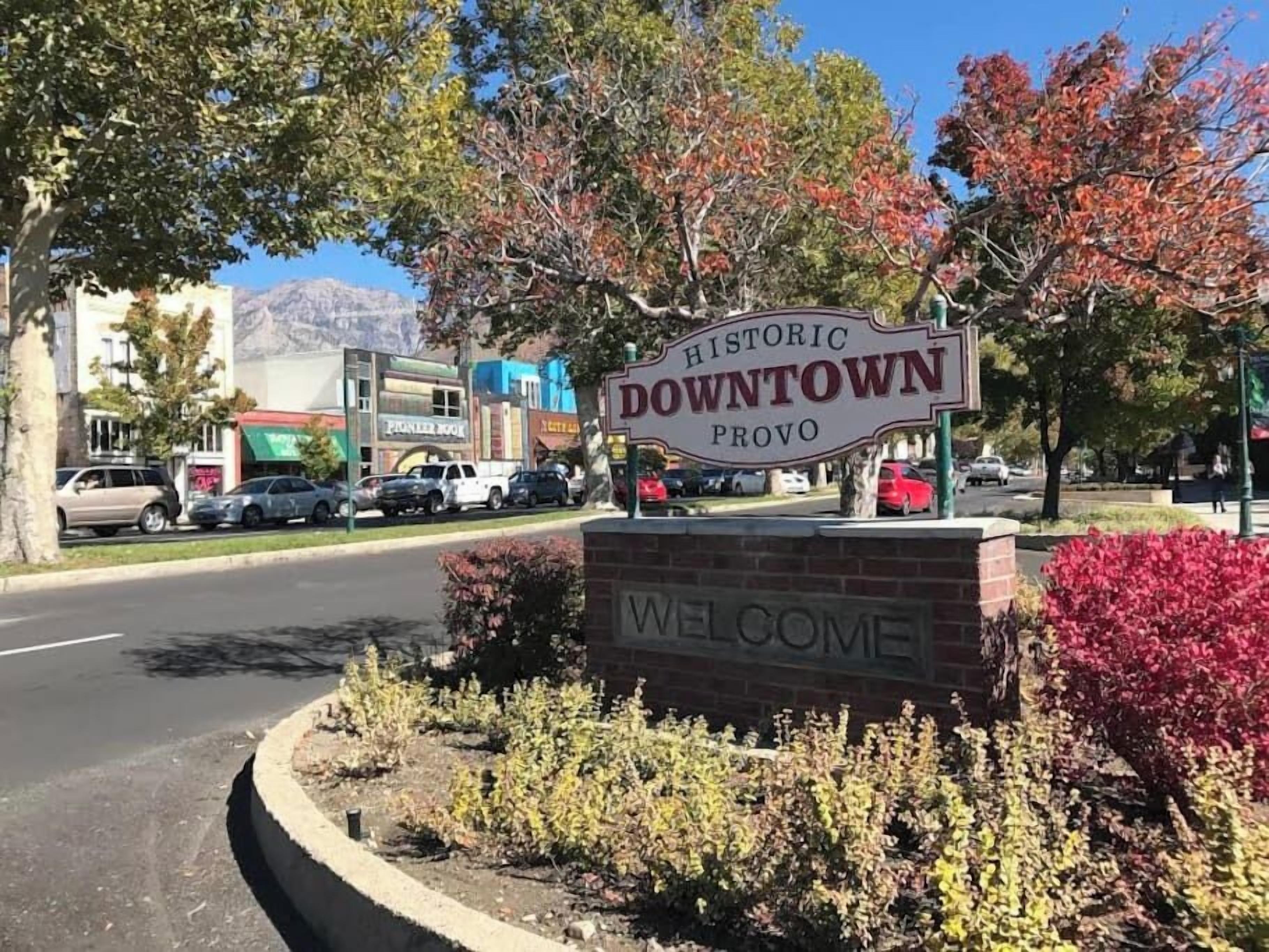 Un letrero de bienvenida a Distrito Histórico de Provo, con una calle despejada y coches estacionados.