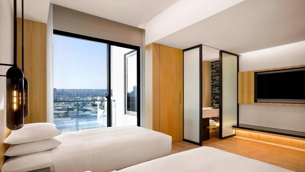 Een moderne hotelkamer met twee bedden, een groot raam met uitzicht op de stad, een televisie en een minibar.