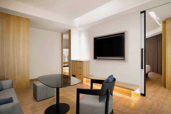Una habitación moderna y luminosa con una mesa redonda, dos sillas, un sofá y un televisor montado en la pared.