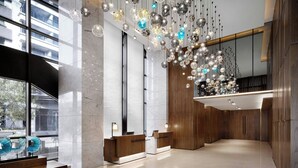 Een moderne lobby met een marmeren receptiebalie, houten lambrisering en een hanglamp.