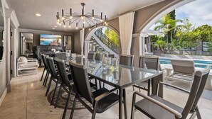 Un espace repas moderne avec une table et des chaises en verre, un escalier et une vue sur la piscine.