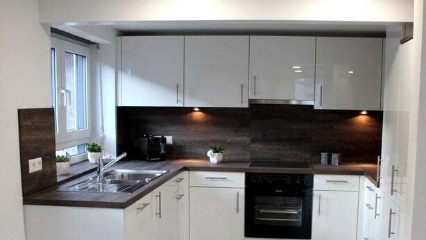 A modern kitchen with white cabinets, a dark backsplash, and a built-in oven.