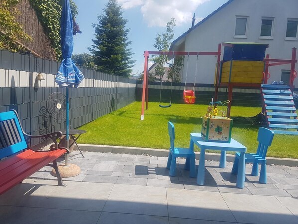Un espacio patio con un columpio, una mesa de juegos y sillas azules.