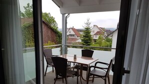 A balcony with a table and chairs, a glass door, and a view of houses in the background.