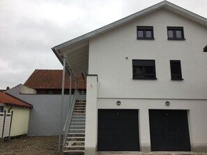 En tvåvåningsbyggnad med en vit fasad och ett sluttande tak. Det finns två svarta garageportar och ett litet fönster på andra våningen.