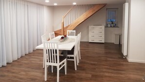 A dining area with a wooden staircase, white chairs, a table with a vase, and a white cabinet.