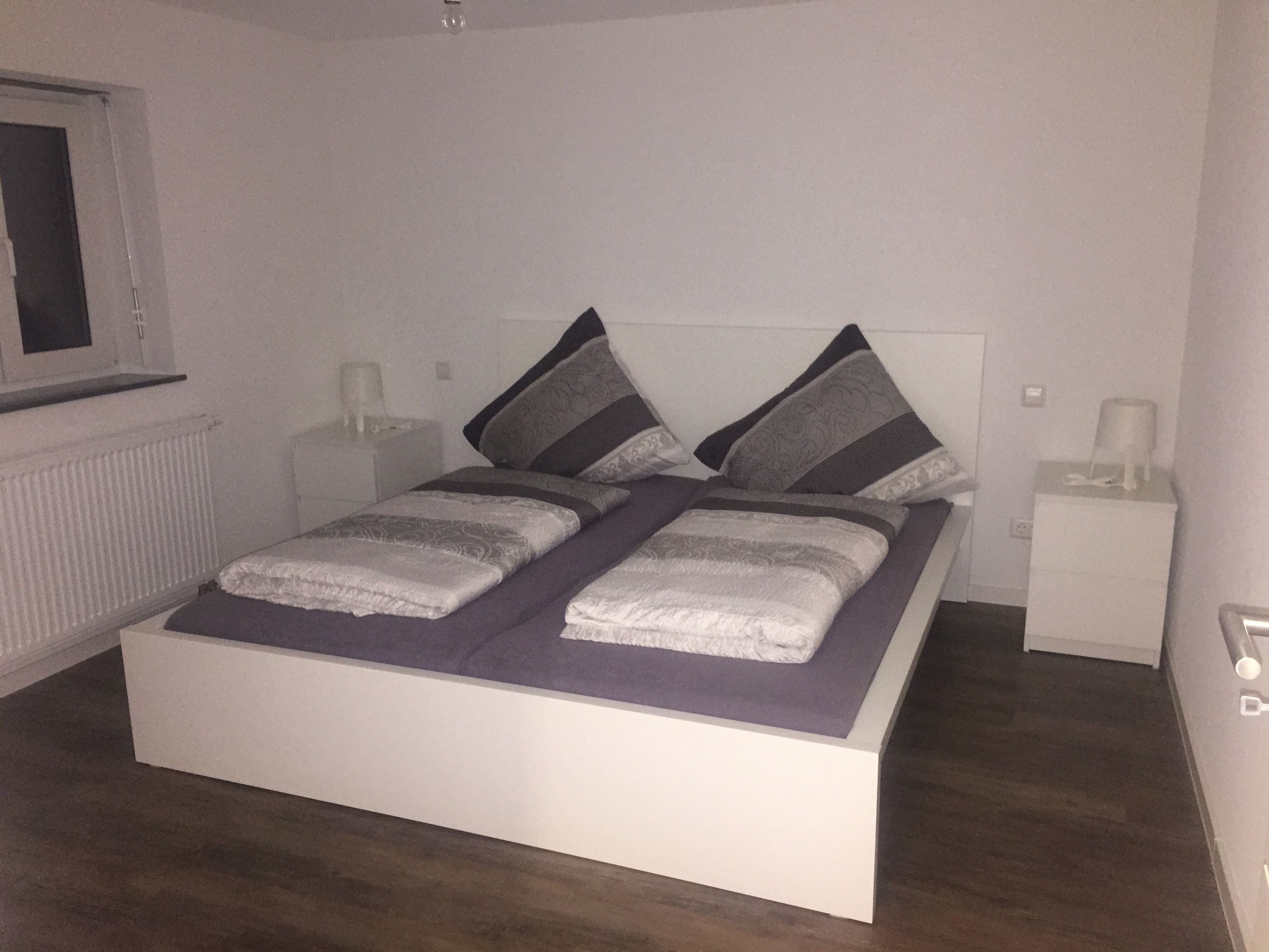 Une chambre à coucher avec un lit, deux tables de chevet, une fenêtre et un radiateur.