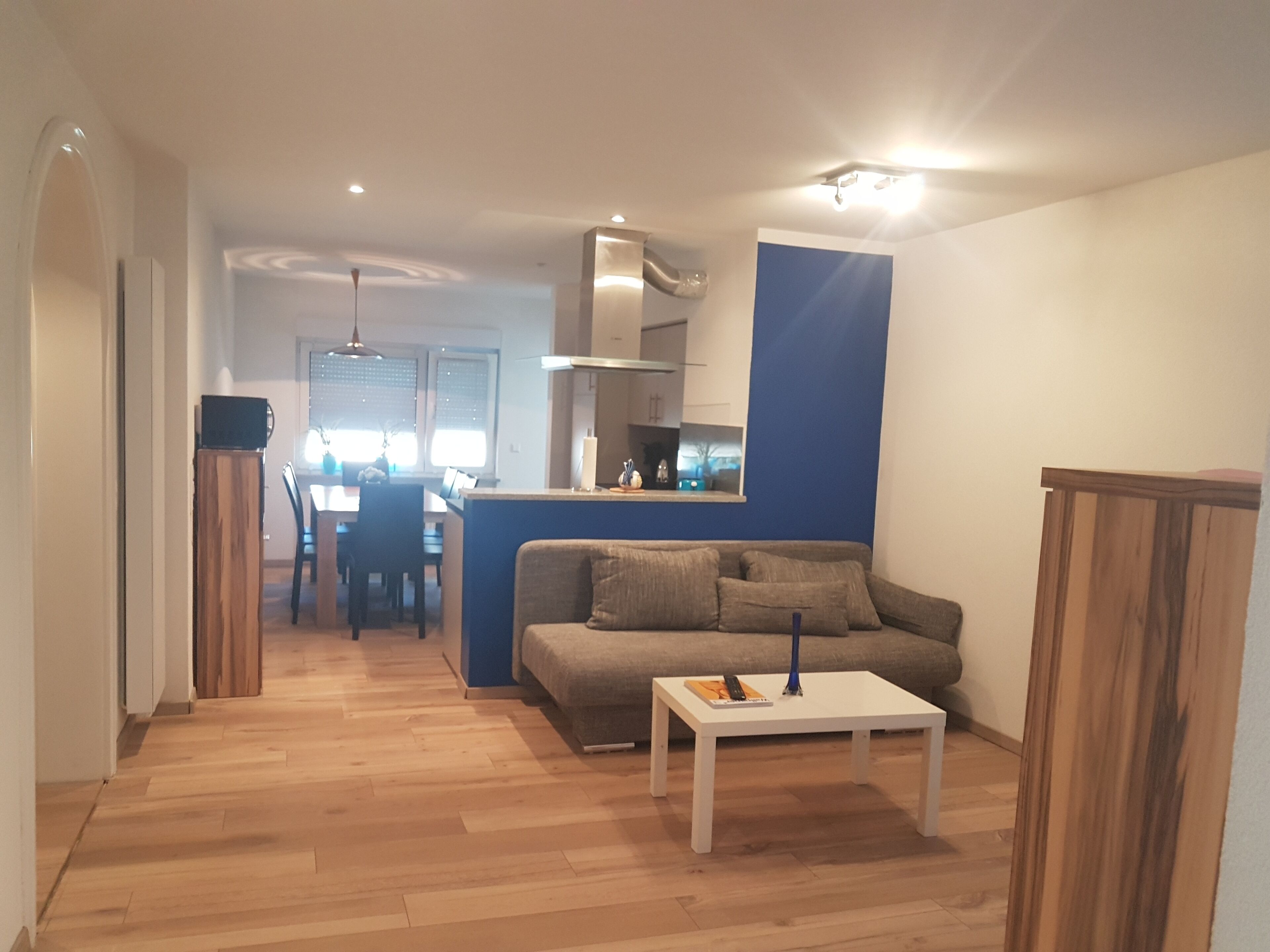 A modern living room with a sofa, a coffee table, and a dining area in the background.