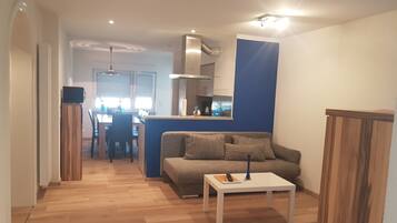 A modern living room with a sofa, a coffee table, and a dining area in the background.