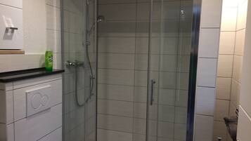 A modern bathroom with a glass-enclosed shower, white tiled walls, and a black countertop.