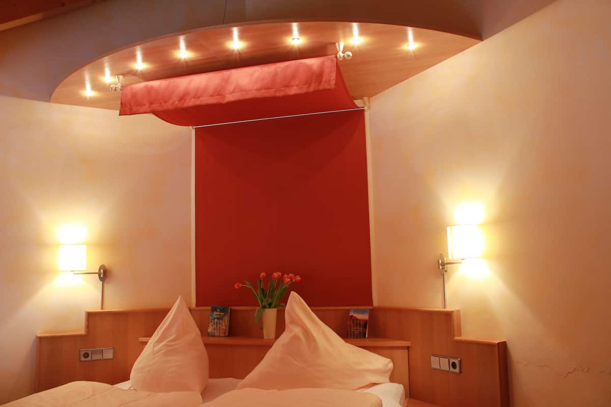 Ein Hotelzimmer mit Bett, Nachttischlampen, einer roten Akzentwand und einer kleinen Vase mit Blumen.