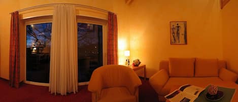 Une chambre d’hôtel confortable avec un escalier en colimaçon, un canapé, un coin lecture et une vue dégagée sur l’extérieur grâce à une grande fenêtre.