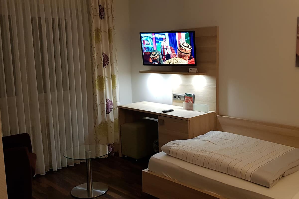 Ein Hotelzimmer mit einem Bett, einem Schreibtisch mit Stuhl, einem an der Wand montierten Fernseher und einem Bild.