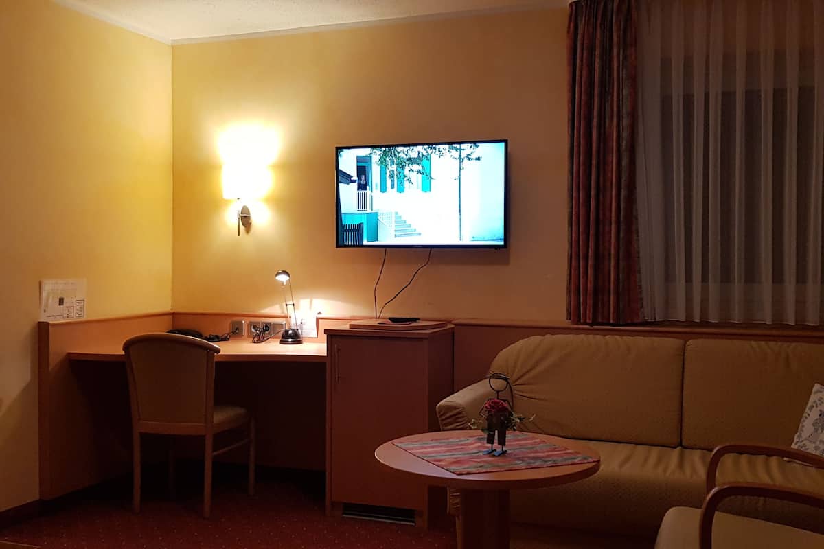 Ein Hotelzimmer mit Schreibtisch, Stuhl, einem kleinen Tisch mit einer Dekoration, einer Couch und einem an der Wand befestigten Fernseher.