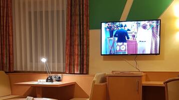 A hotel room with a bed, a desk, a chair, a TV, and a window with curtains.