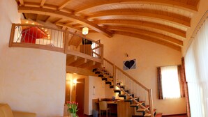 A spacious living area with a wooden staircase, a dining area, and a cozy seating arrangement. - Hotel Fröhlich (Kaiserslautern)