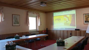 A conference room with a long table, chairs, a projector screen displaying a hotel advertisement, and a window with curtains.