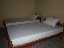 Cama de casal com cabeceira e peseira de madeira, duas almofadas e mesa de cabeceira com abajur.