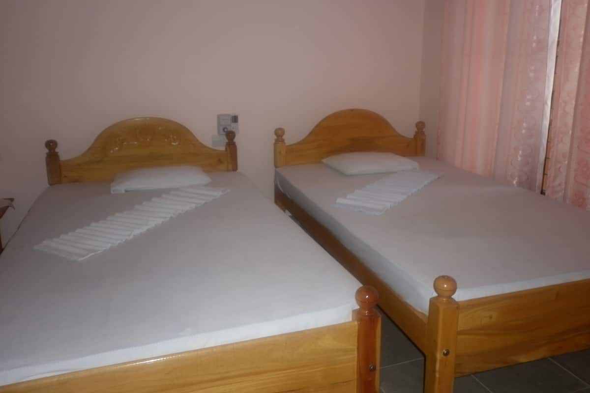Two wooden beds with white linens and a small wall-mounted device.