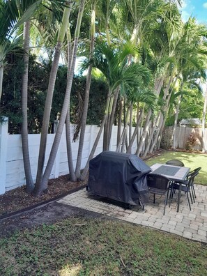 A patio area with a covered grill, a table and chairs, and a white fence with palm trees in the background. - BEACHFRONT, OCEAN! 2 BEDRMS, 3 BATHRMS, Discounts for longer stay APP-VRR1500402 (Fort Lauderdale)