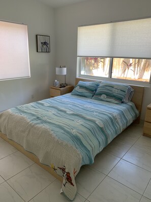 A bedroom with a bed, a nightstand, a lamp, a window with blinds, and a wall-mounted picture. - BEACHFRONT, OCEAN! 2 BEDRMS, 3 BATHRMS, Discounts for longer stay APP-VRR1500402 (Fort Lauderdale)