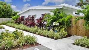 Une maison moderne dotée d’un toit plat, entourée d’une végétation tropicale luxuriante et d’une clôture en bois.