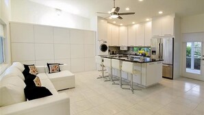 Une cuisine moderne avec des meubles blancs, un îlot central doté de tabourets de bar et un four encastré.