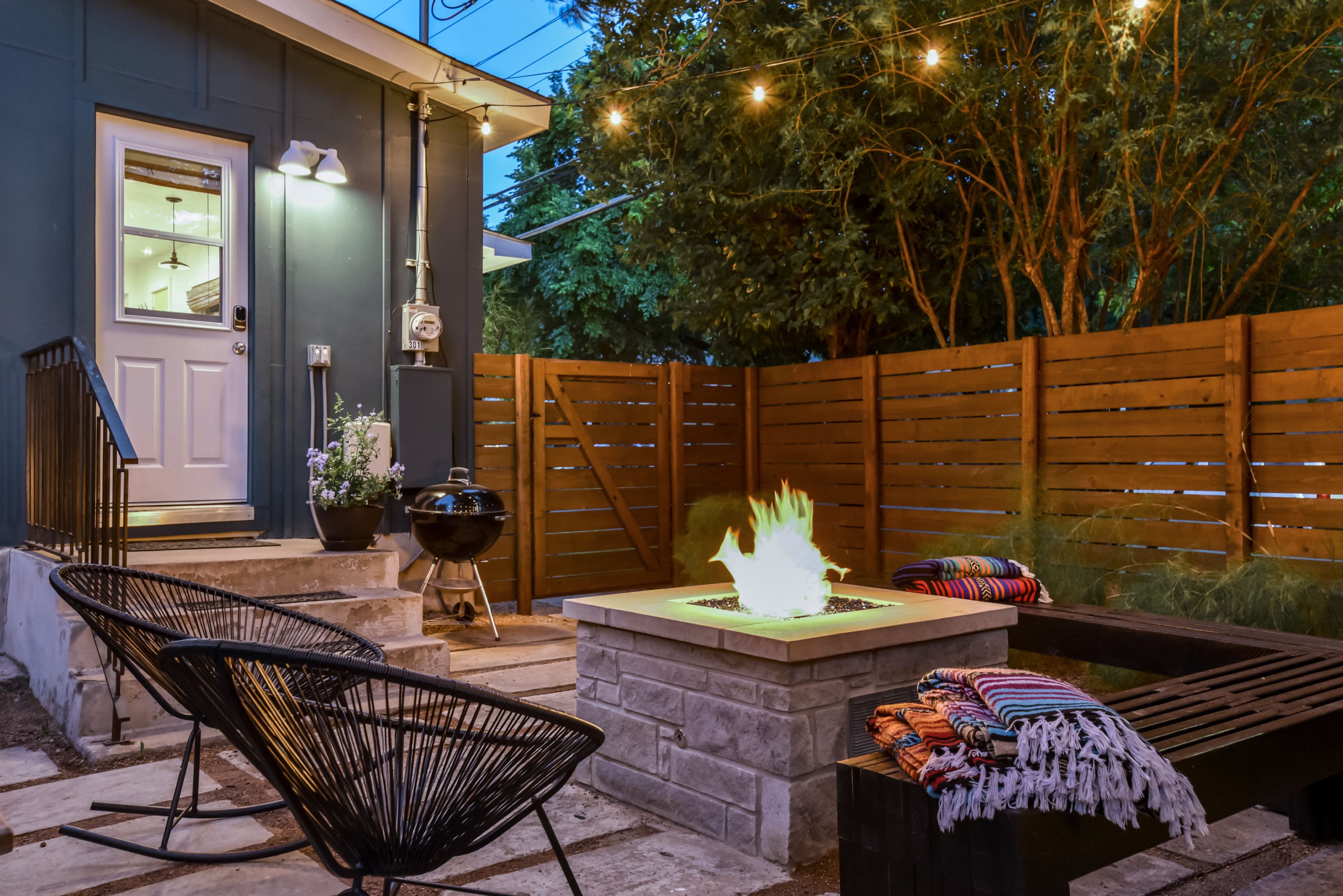 Un patio con una fogata, mobiliario exterior y una valla de madera.
