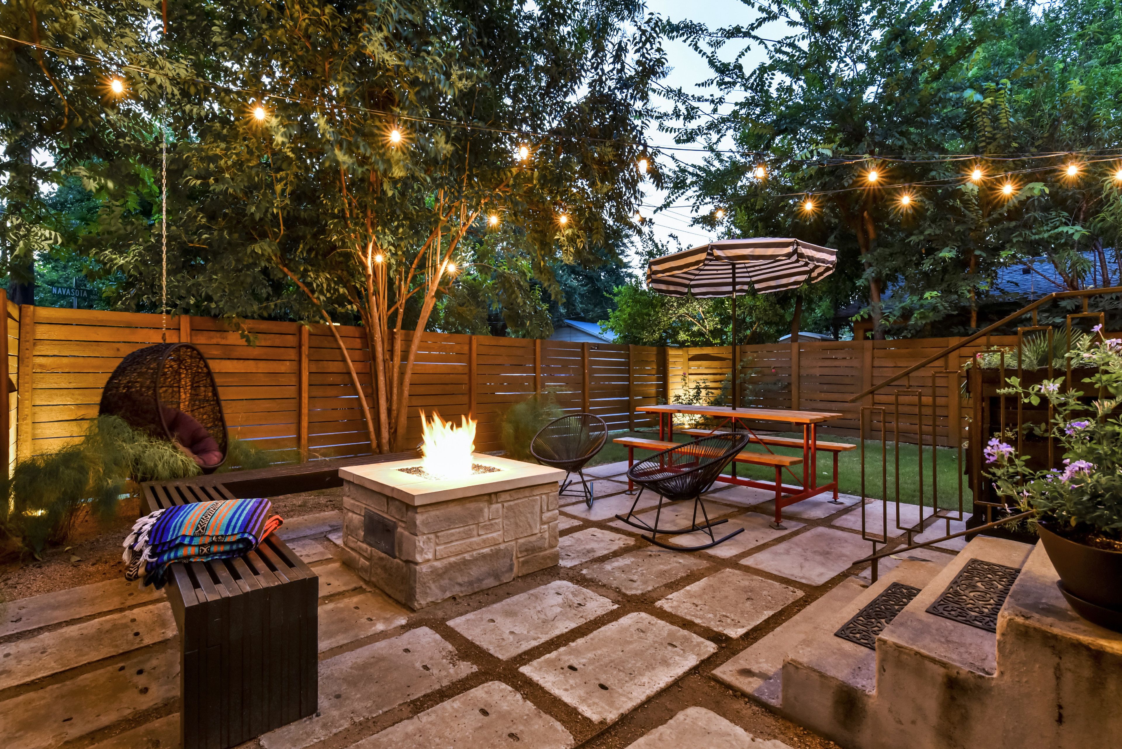 A patio with stone flooring, a fire pit, outdoor furniture, string lights, and a wooden fence.
