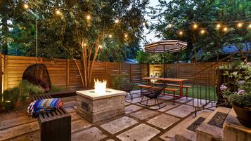 A patio with stone flooring, a fire pit, outdoor furniture, string lights, and a wooden fence.
