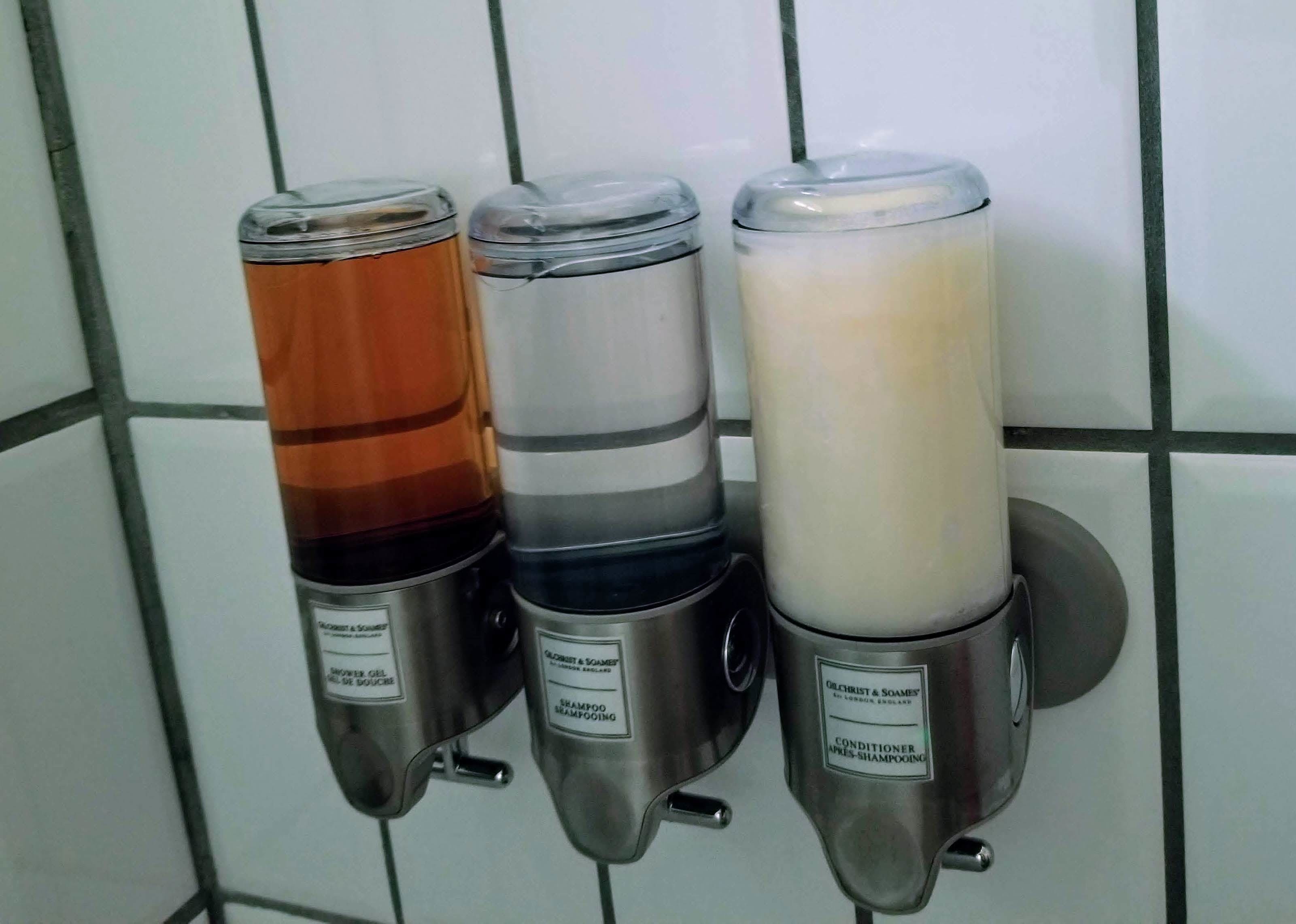 Trois distributeurs de shampoing dans une salle de bain carrelée.