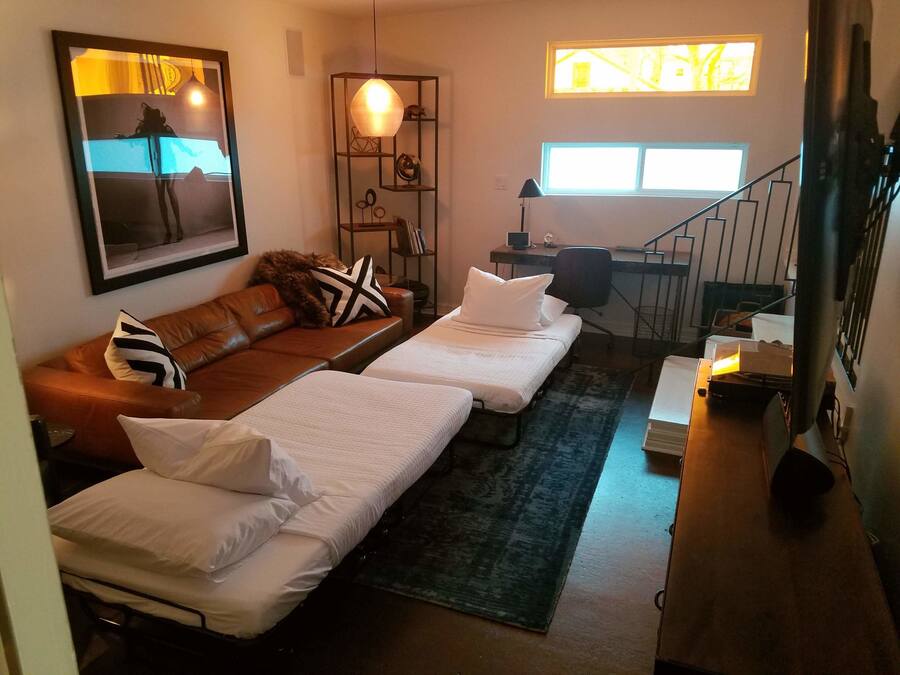Una habitación acogedora con dos camas individuales, un sofá de cuero marrón, un escritorio con silla y un amplio ventanal que proporciona luz natural.